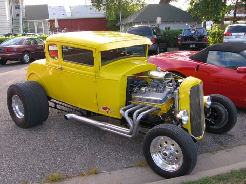 1989 Ford Mustang - A bright yellow hot rod coupe is parked next to a red convertible, its powerful engine and custom exhaust.
