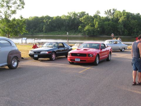 1989 Ford Mustang - Two Ford Mustangs, one red and one black, are parked at an outdoor car show.