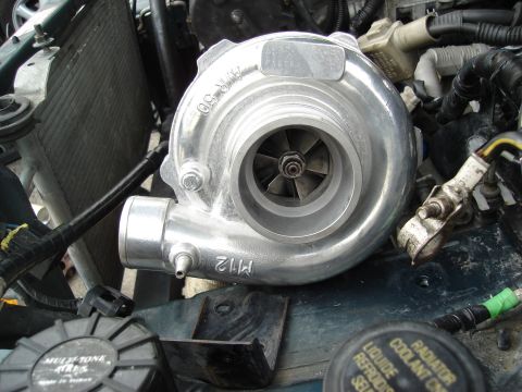 1995 Mazda MX-6 - Close-up of a turbocharger in an engine bay, showing internal fan blades and external markings.