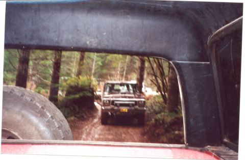 1989 Ford Bronco - A brown Ford Bronco navigates a muddy forest road, viewed from the interior of another vehicle.