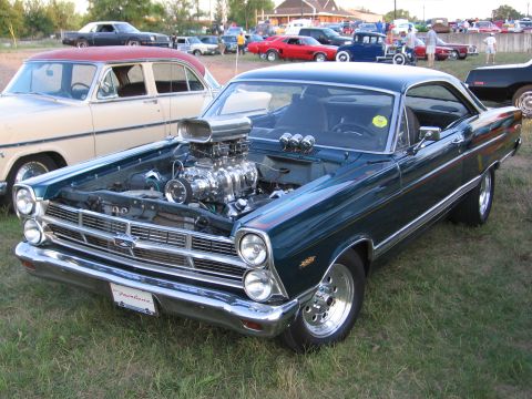 1989 Ford Mustang - A classic car with a prominent supercharger is displayed at an outdoor event with other vehicles visible.