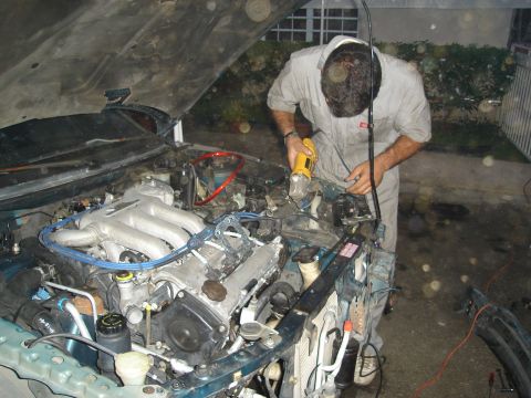 1995 Mazda MX-6 - A person works on the engine of a 1995 Mazda MX-6, with the hood open.