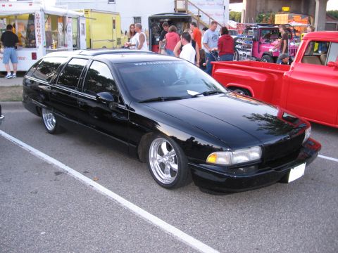 1989 Ford Mustang - A black station wagon with custom chrome wheels is parked at a car show.
