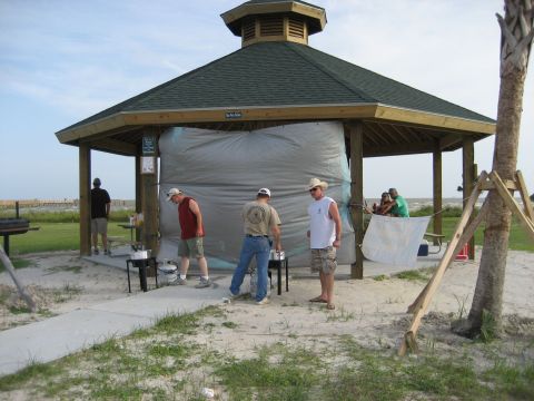 1986 Ford Bronco - People are gathered around a beach pavilion on a sunny day, with a tarp covering a section of the structure.