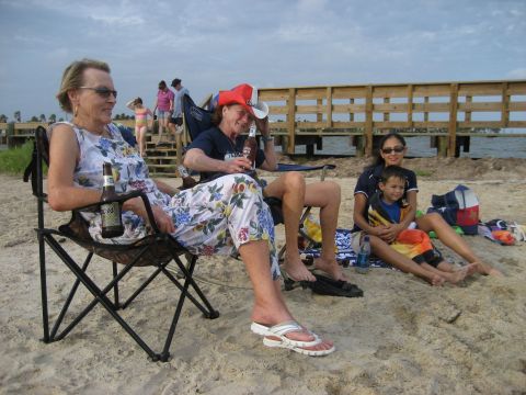 1986 Ford Bronco - A group enjoys a day at the beach, with a wooden pier in the background and a cloudy sky overhead.