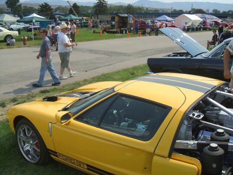 1974 Ford Ranchero - A yellow 2005 Ford GT with racing stripes is displayed at a car show, with other vehicles and tents in the background.