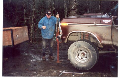 1989 Ford Bronco - A man uses a jack to lift a maroon Ford Bronco in a wooded area.