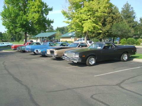 1974 Ford Ranchero - Several classic cars are parked in a lot under trees, including a black Ford Ranchero in the foreground.