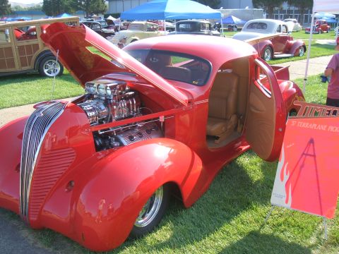 1974 Ford Ranchero - A custom red hot rod with its hood and door open sits on display at a car show.