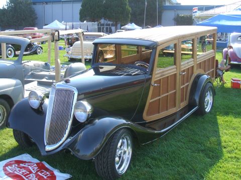 1974 Ford Ranchero - A classic black woody wagon with a prominent chrome grille and custom wheels is displayed at an outdoor car show.