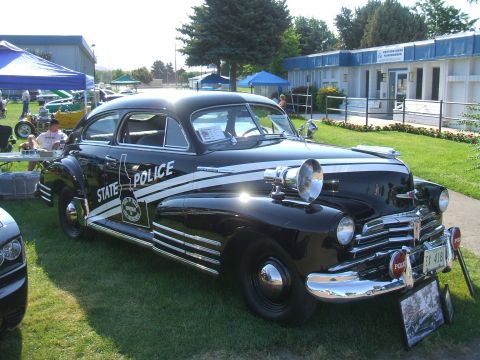 1974 Ford Ranchero - A classic black police car with white stripes and a spotlight is parked on a grassy lawn.