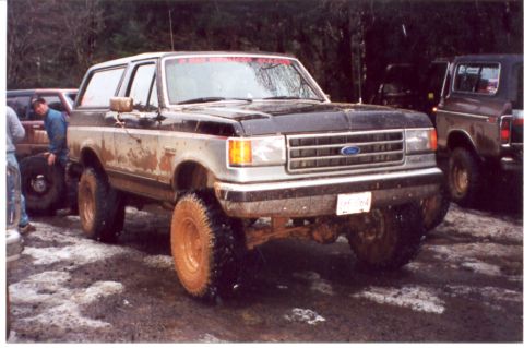 1989 Ford Bronco - Muddy 1989 Ford Bronco parked off-road with another vehicle behind it.