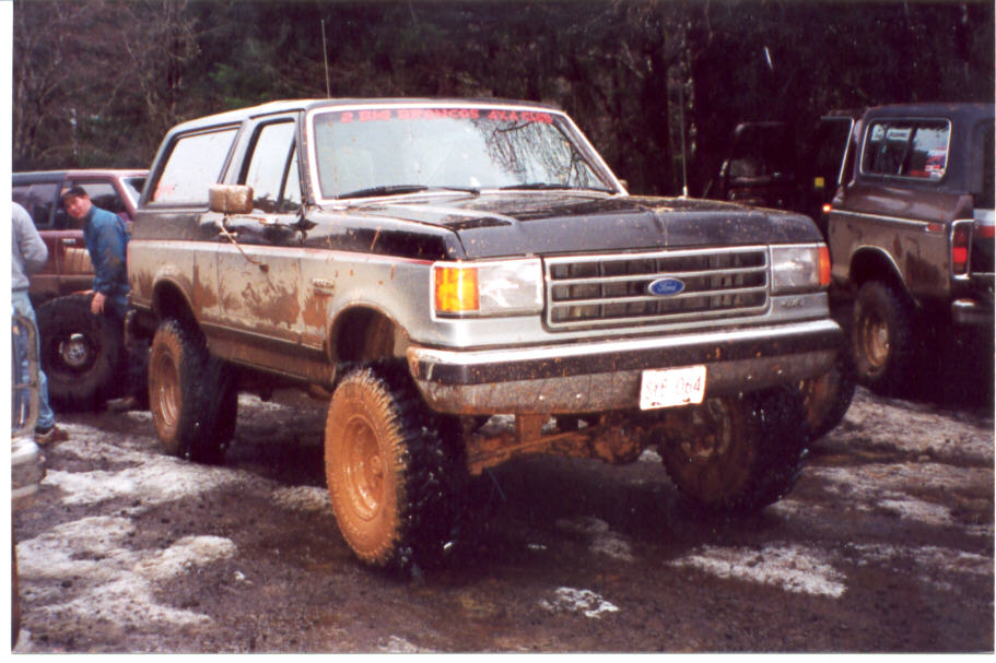 Muddy two-tone lifted Ford Bronco with 4x4 club windshield banner in a mud lot