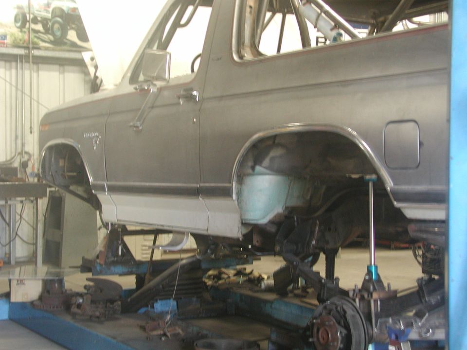 Gray Ford Bronco body on shop lift, wheels and fenders removed, axle and parts underneath