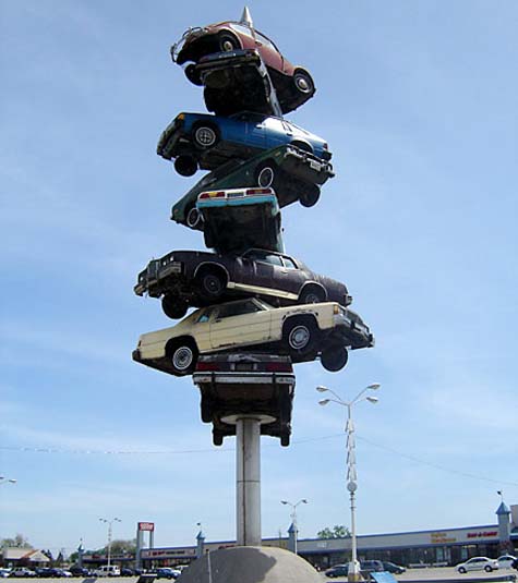 1978 Ford Mustang II - Multiple cars are stacked vertically on a pole in an outdoor scene.