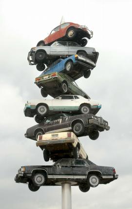 1978 Ford Mustang II - Several cars are stacked vertically on a pole against a cloudy sky.