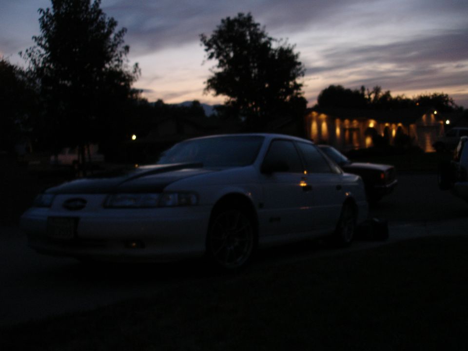 White 1993 Ford Taurus sedan with a black hood stripe parked at dusk