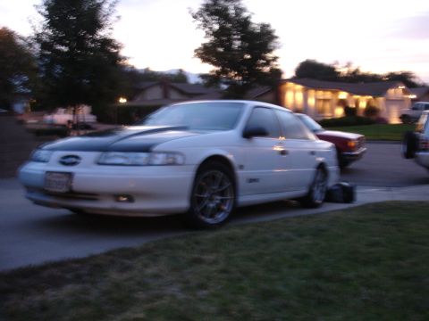 1993 Ford Taurus - A white 1993 Ford Taurus with a black hood and aftermarket wheels is parked on a suburban street.
