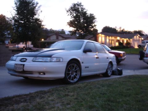 1993 Ford Taurus - White 1993 Ford Taurus with a black hood and aftermarket wheels is parked on a street.