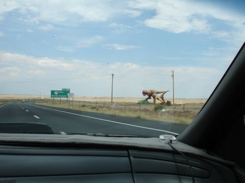 1993 Ford Taurus - A roadside dinosaur statue stands near a highway sign pointing towards Kayenta Canyon.
