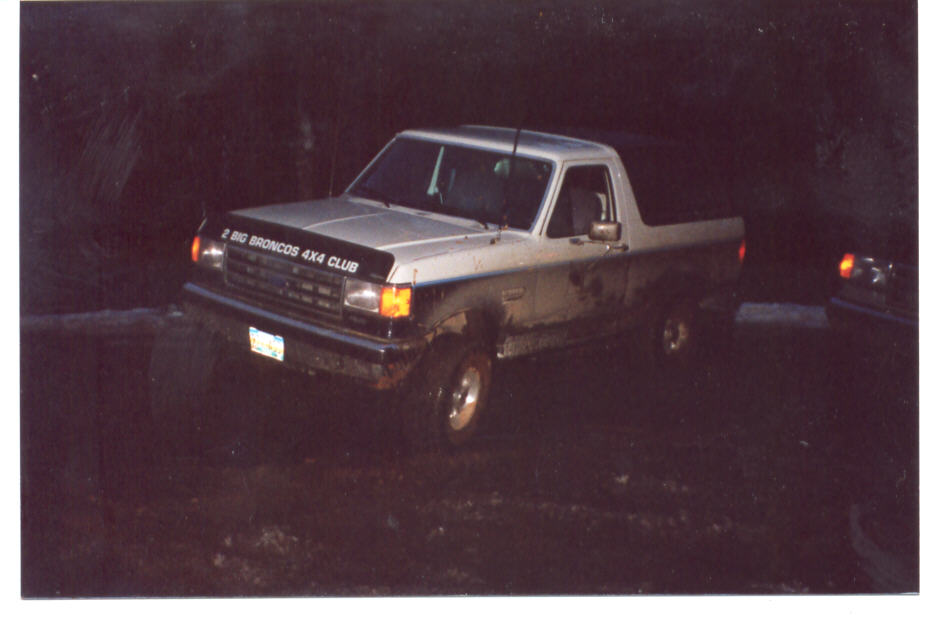 Two-tone Ford pickup with a 4x4 club banner in a dark muddy field at night