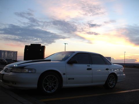 1993 Ford Taurus - Side view of a white 1993 Ford Taurus sedan with a black hood stripe during sunset.