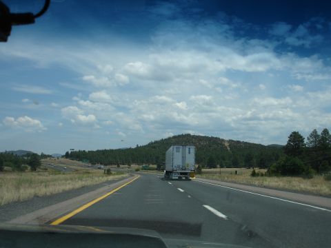 1993 Ford Taurus - A semi-trailer truck travels down a highway, passing through a rural, wooded area.