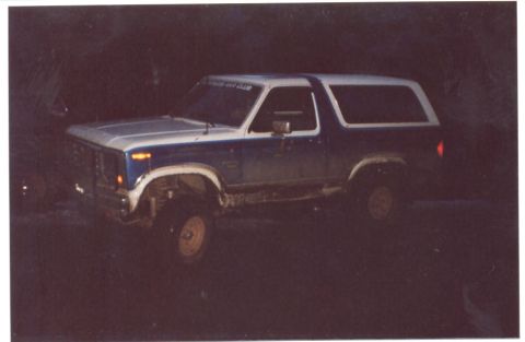 1989 Ford Bronco - A lifted Ford Bronco is parked in a dark, outdoor setting, possibly off-road.