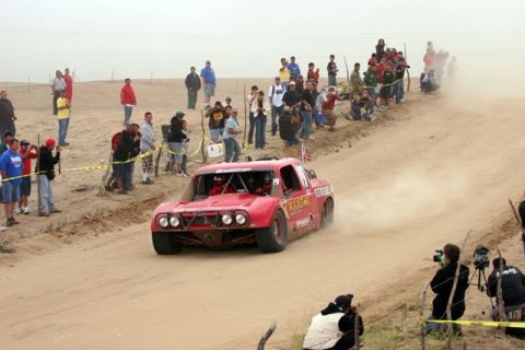 1996 Ford Bronco - A red off-road race truck competes on a dusty dirt track, observed by a crowd of onlookers.