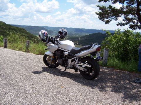 2003 Suzuki Bandit S - A white Suzuki Bandit S motorcycle is parked on a gravel road with a scenic view of rolling hills and a cloudy sky.