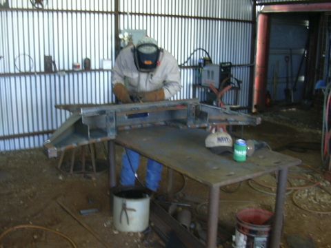 1995 Ford Bronco - A person in welding gear works on a custom metal front bumper in a corrugated metal workshop.