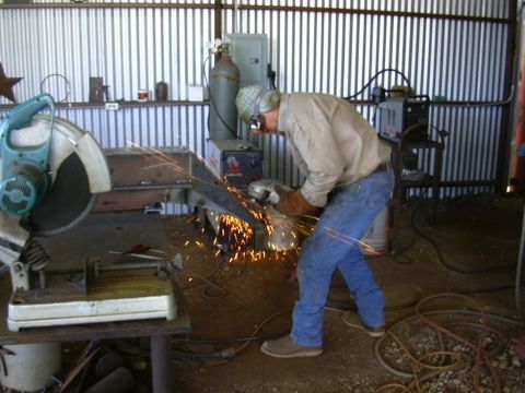 1995 Ford Bronco - A worker uses an angle grinder on a metal piece inside a workshop, with sparks illuminating the scene.