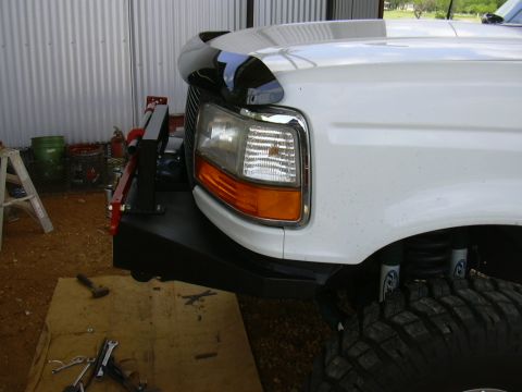 1995 Ford Bronco - White Ford F-Series truck with a custom front bumper and large off-road tire is shown from the front quarter angle.