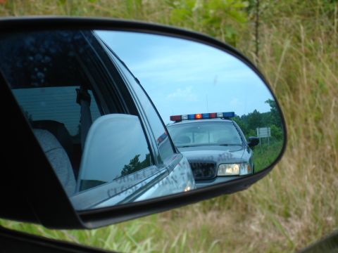 1993 Ford Taurus - A police car with its light bar illuminated is seen in the reflection of a side mirror.