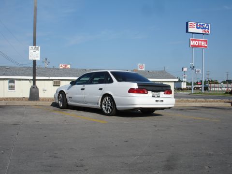 1993 Ford Taurus - A white 1993 Ford Taurus sedan is seen from the rear, parked in a lot with a motel sign in the background.