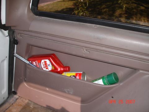 1995 Ford Bronco - Door panel storage compartment holds various automotive fluids and a spray can.