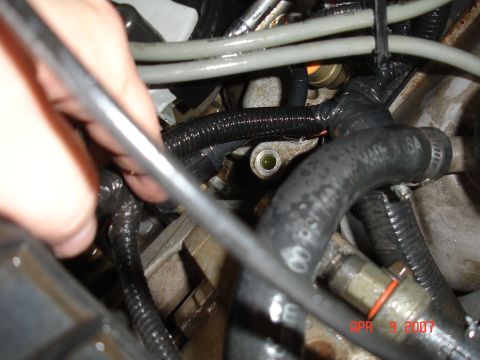 1995 Ford Bronco - Engine bay detail with hoses, wiring, and a hand working on a component.