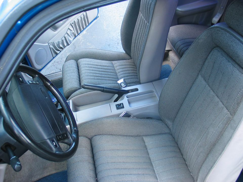 Blue 1990 Ford Mustang interior showing grey fabric seats, dashboard, steering wheel, and center console