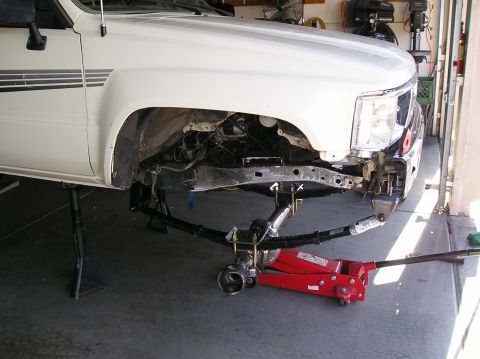 1986 Toyota Hilux - The front suspension of a white truck is disassembled, with leaf springs and other parts laid out for repair.