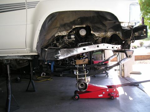 1986 Toyota Hilux - Rear underside of a white Toyota pickup on jack stands with the bed removed, showing new leaf-spring packs, shackles and shocks bolted to t…