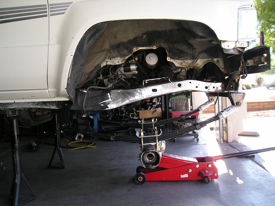 Underside of white Toyota pickup on jack stands showing leaf springs and frame