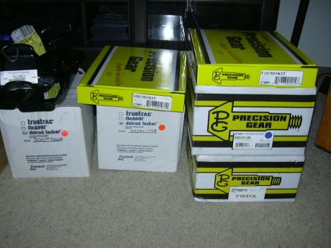 1995 Ford Bronco - Boxes of automotive parts, including Precision Gear and Truetrac Detroit Locker, are stacked on a carpeted floor.