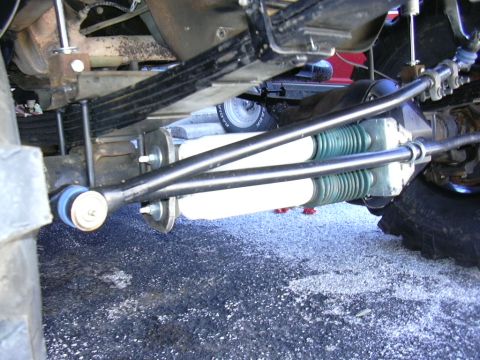 1995 Ford Bronco - Close-up of the undercarriage shows a solid axle swap with dual shocks and leaf springs, indicating significant suspension modification.