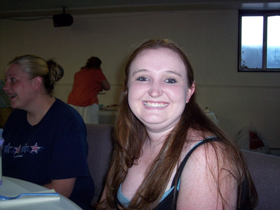 Woman with long brown hair smiling, another woman with blonde hair laughing to her left. People in background