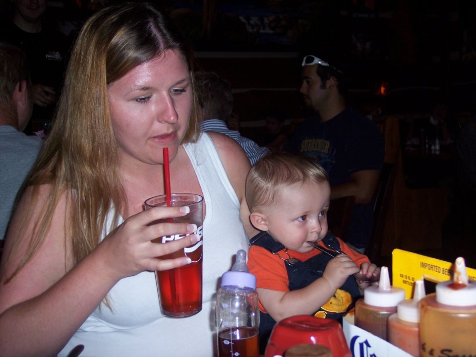 Woman drinks from a Pepsi cup while a baby eats with a fork