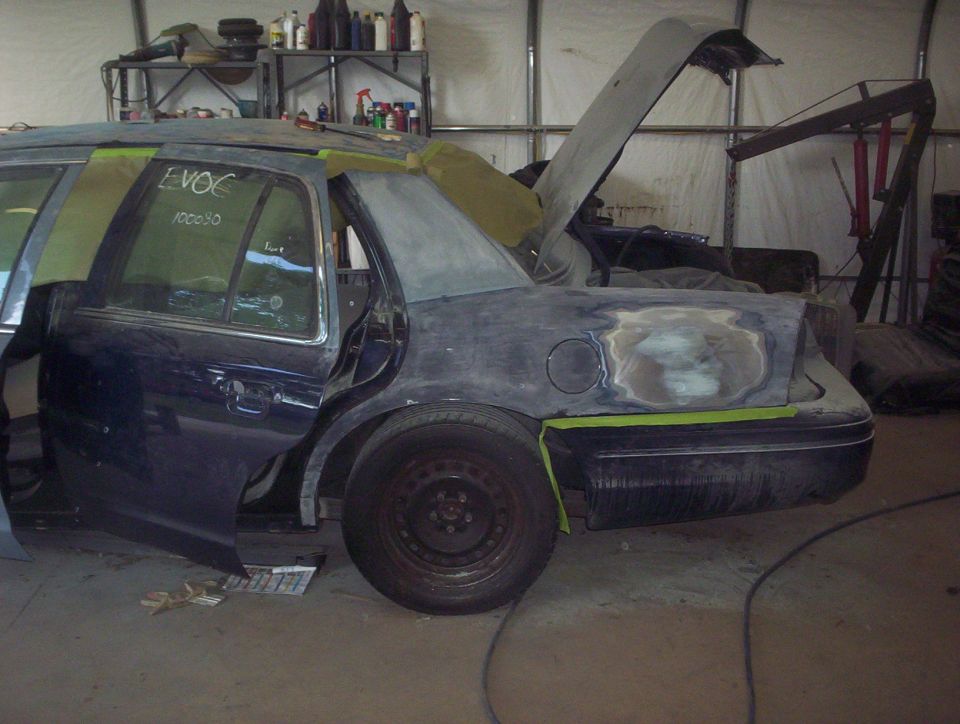 Dark blue 1998 Ford Crown Victoria undergoing bodywork, rear quarter panel being prepped