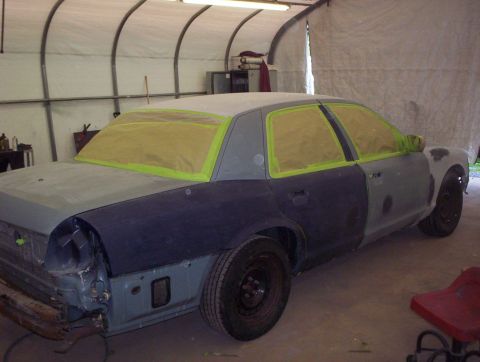 1998 Ford Crown Victoria - A 1998 Ford Crown Victoria is prepped for painting in a workshop, garage with yellow masking tape on the windows.