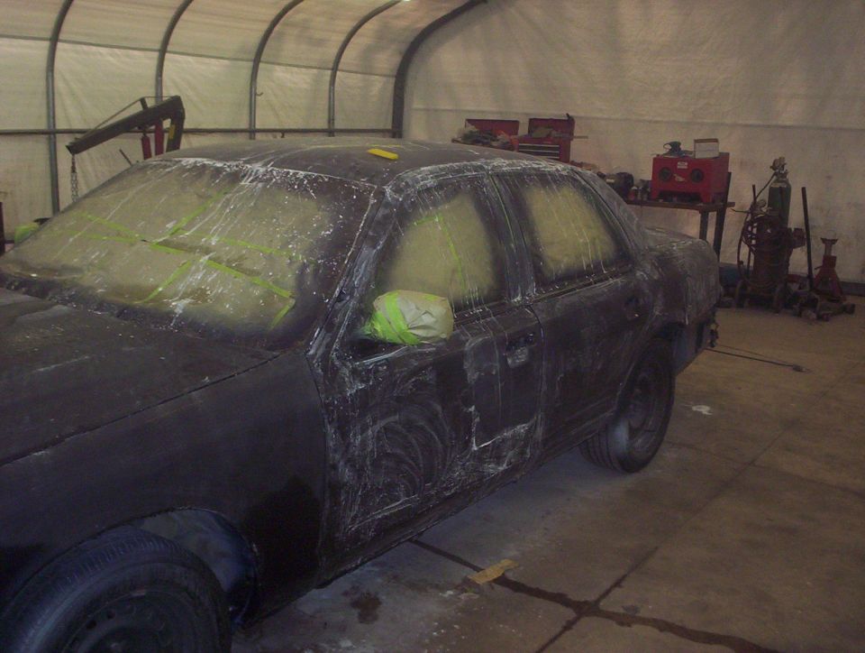 Black 1998 Ford Crown Victoria in a garage, prepped for paint with masking tape on windows