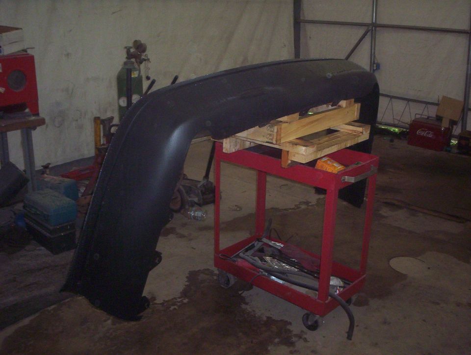 Black bumper resting on a red cart with wooden supports in a garage