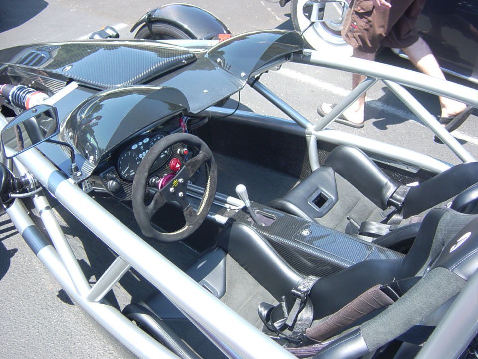 Interior of a lightweight sports car with a roll cage, racing seats, and a steering wheel
